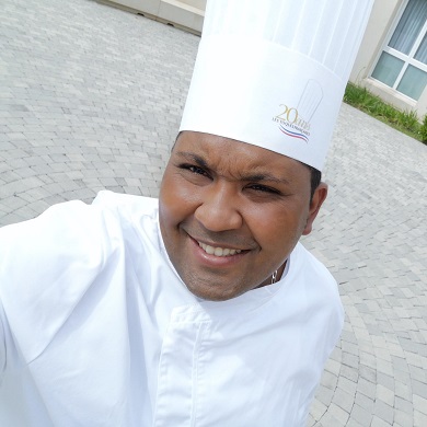Julien stands in a courtyard wearing a white chef's hat.