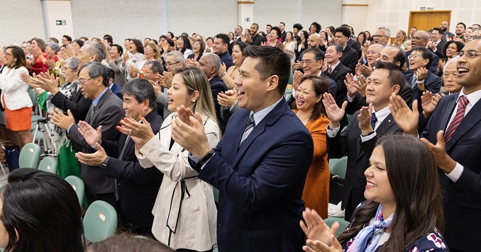 Audience members in a full hall standing and clapping.