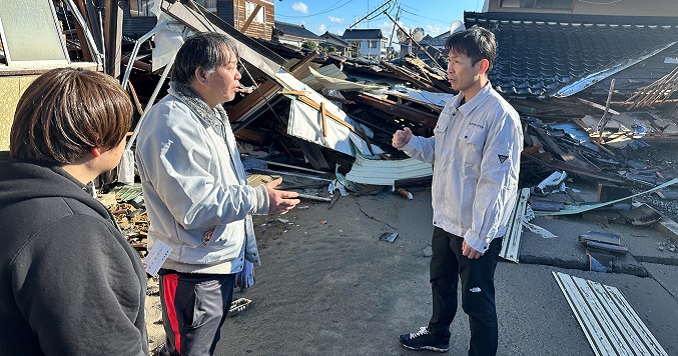 三人站在被能登地震摧毀的房屋殘骸前。