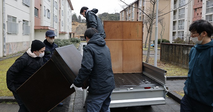 A group of people carrying damaged furniture to a car.