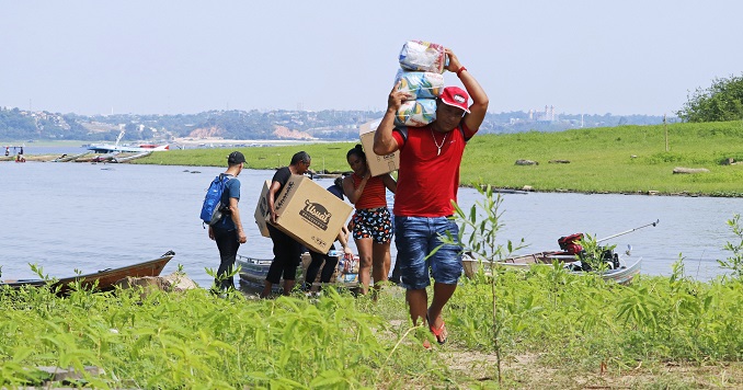 Un grupo de hombres transportan suministros de socorro desde una embarcación pequeña y caminan tierra adentro.