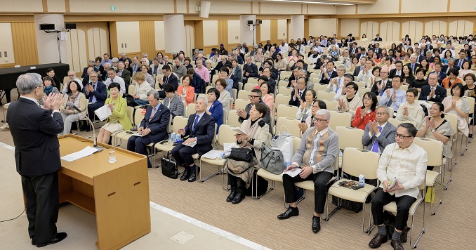 一大群人坐在会堂里聆听讲台上的演讲者讲话。