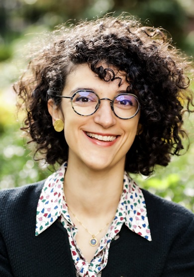 Mujer con pelo rizado y gafas, sonríe mirando a la cámara.