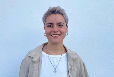Young woman with short, pinkish hair smiling at the camera.