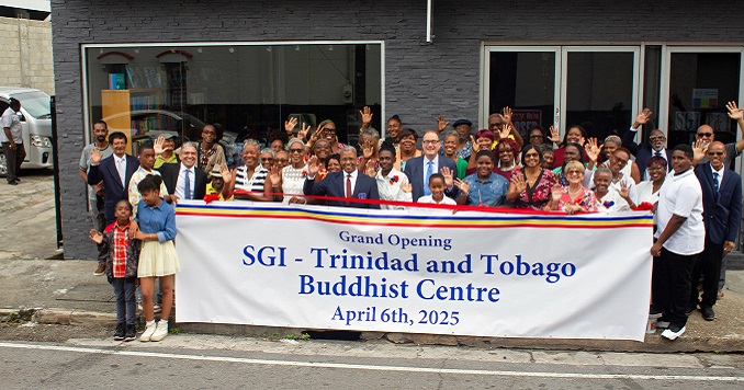 People smiling and waving, holding a banner outside a modern building.
