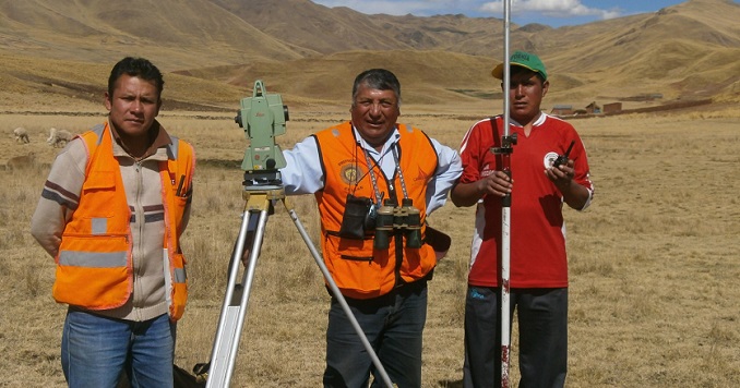Three men in a mountainous area standing next to a tool to create a path for a transmission line.