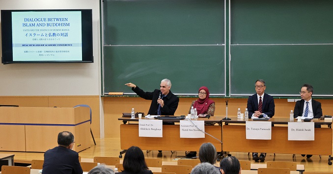 Cuatro personas sentadas en una mesa frente a un público en una sala de conferencias.