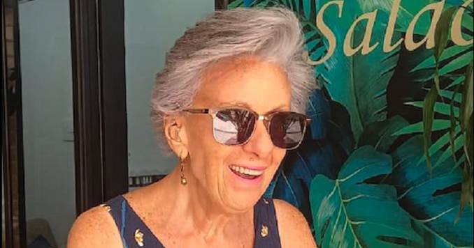 Una mujer con gafas de sol sonríe ante de un fondo pintado con hojas.