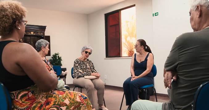 Varias personas sentadas en sillas en una pequeña sala mantienen una conversación.