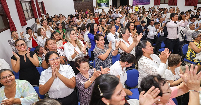 Many people applauding and smiling at a meeting in a conference room.