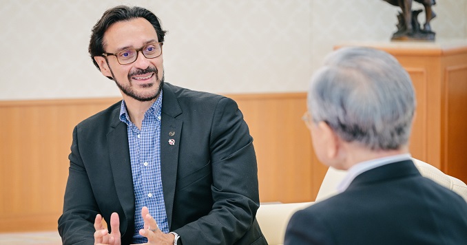 Un hombre con gafas y barba hablando animadamente con otra persona.