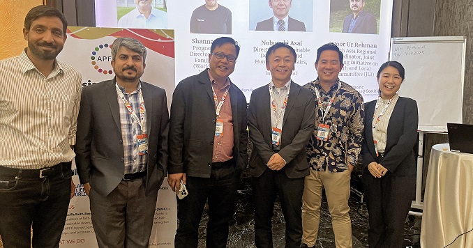 Six people in front of a large screen, smiling at the camera.