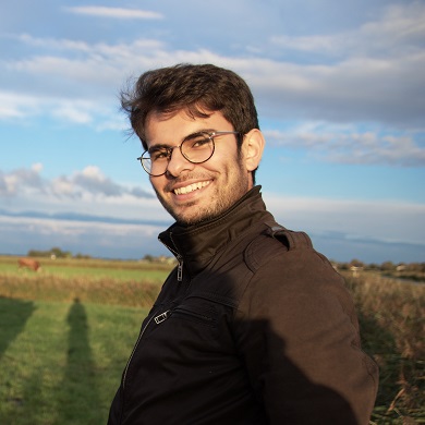 男子站在綠色草坪上與兩頭牛合影。