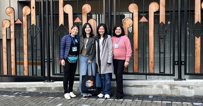 Four women standing together in front of an ornate railing.