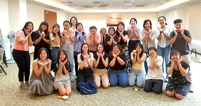 A group of young women pose for a commemorative photo with their hands framing their faces.