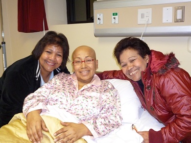 A woman sitting in her hospital bed with two women by her side.