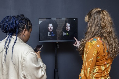 Two people, one looking at a phone and the other at a screen in front of them.