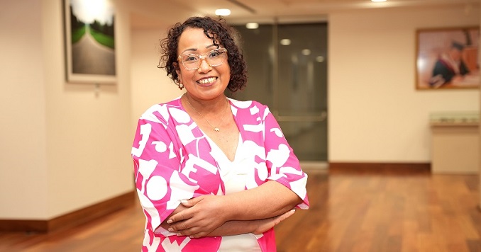 A woman in brightly colored clothes stands with her arms crossed, smiling at the camera.