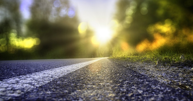 A tree-lined road with bright sunlight at the end.