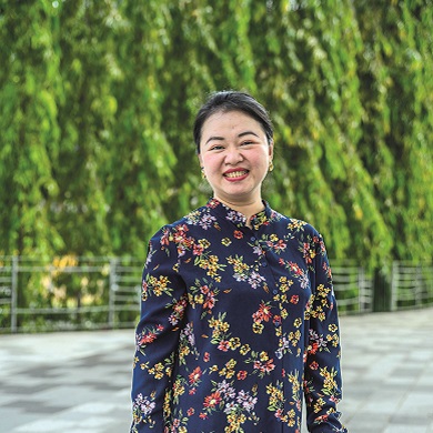 Szi Hean smiles in front of lush greenery, wearing a purple floral-print top.
