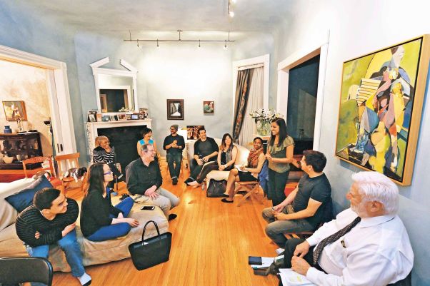 A diverse group of around a dozen people in discussion in the living room of a large house