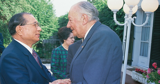 Ikeda and Huyghe stand face-to-face clasping each other’s hands outside a building