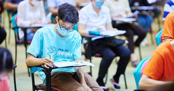 People seated in a big room taking a written exam