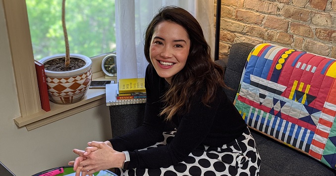 Jenny sitting on her couch next to a colorful pillow and smiling